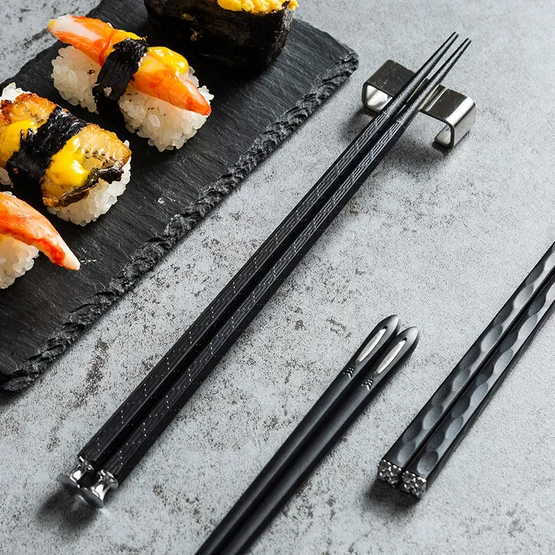 Schwarze Essstäbchen auf grauem Untergrund mit Sushi und stilvollem Zubehör, Küchenutensilien