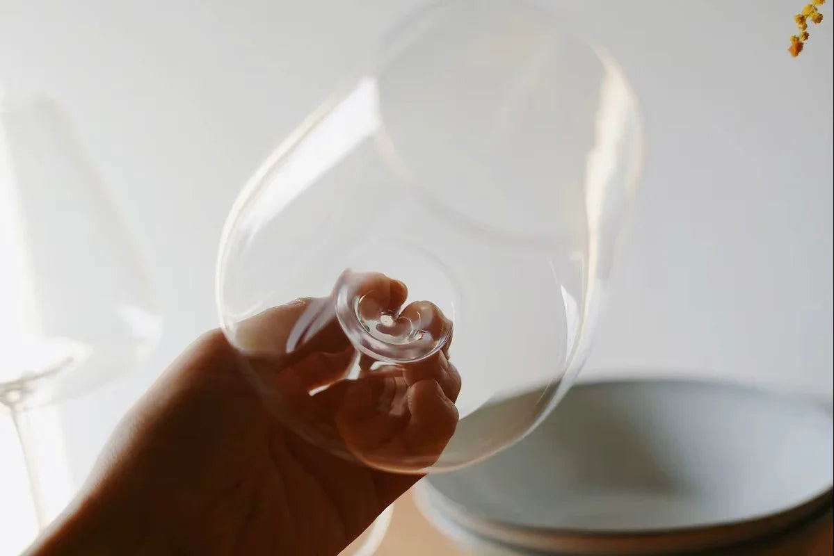 Hand hält hochwertiges Weinglas vor neutralem Hintergrund, stilvolle Küchenutensilien