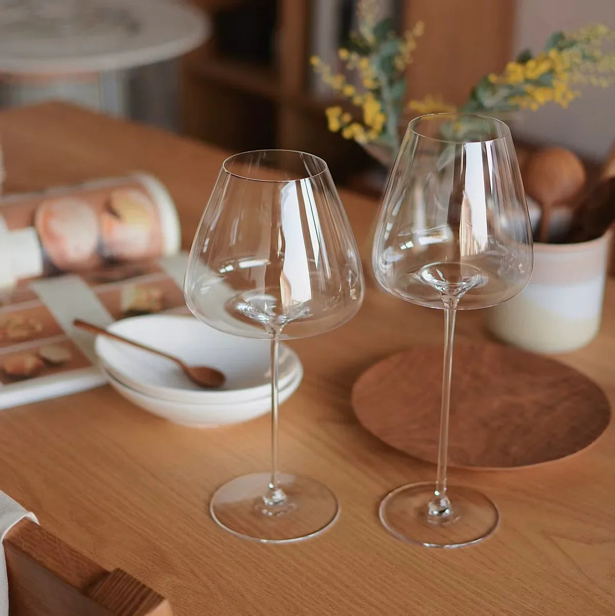 Zwei hochwertige Weingläser auf Holztisch mit Schalen, Kochlöffel und stilvoller Küchendeko