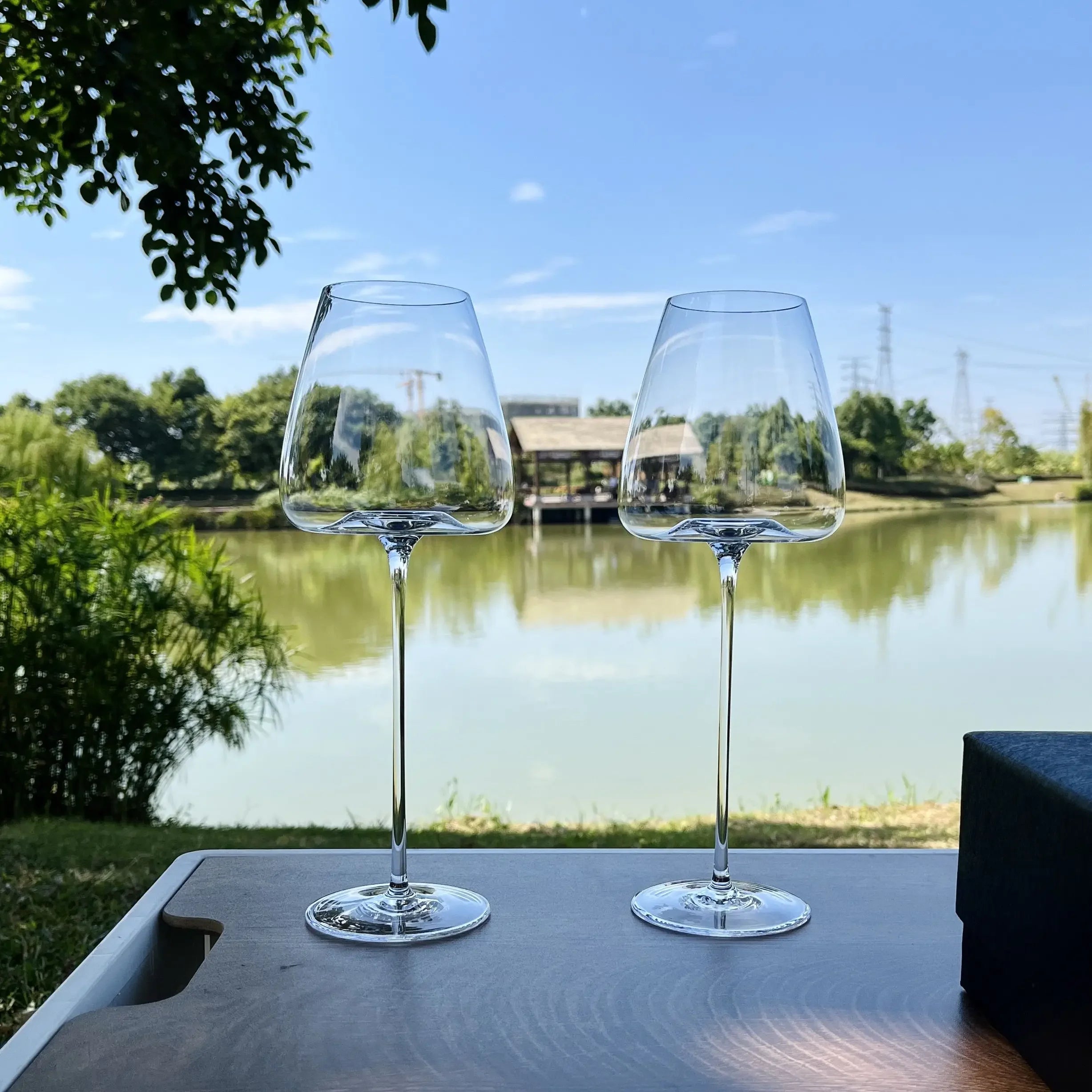 Zwei elegante Weingläser auf Holztisch am See, exklusive Küchenaccessoires bei Kochschein