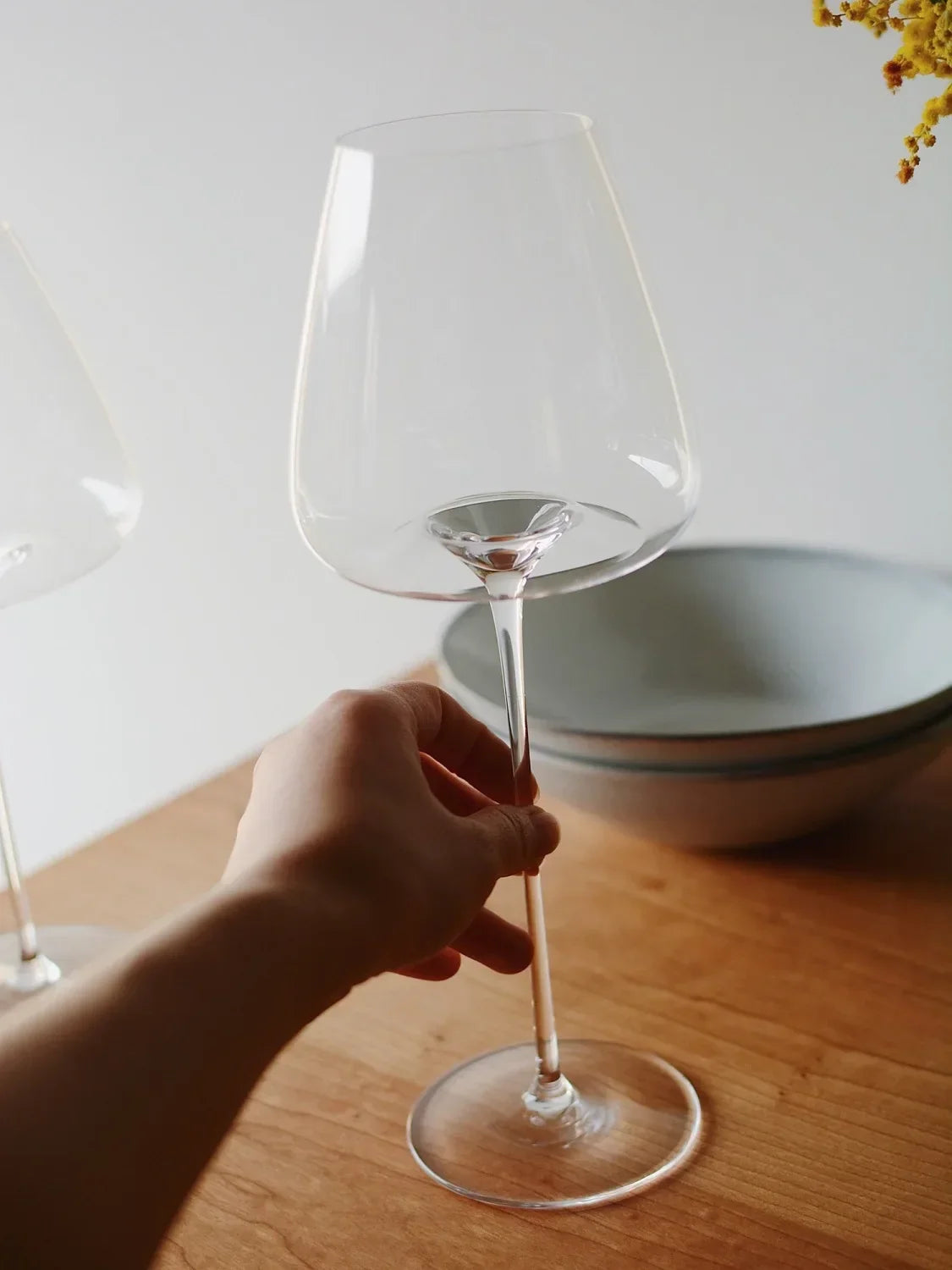 Hand hält elegantes Weinglas auf Holztisch, moderne Küchenschale im Hintergrund