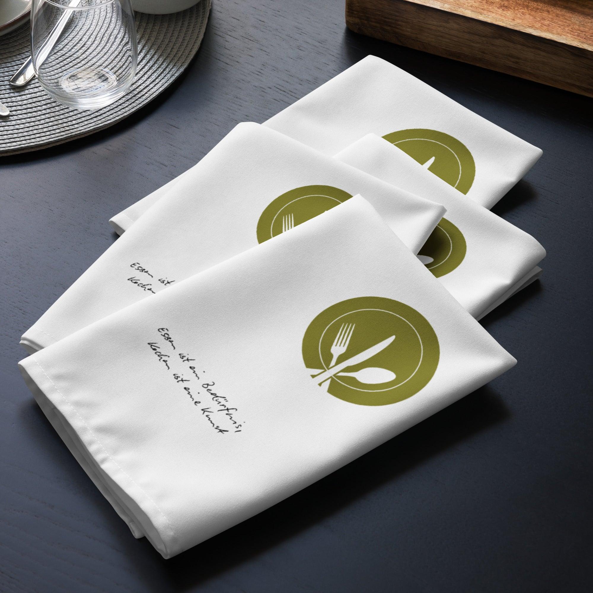 Vier weiße Stoffservietten mit Besteck-Motiv und Schriftzug, stilvoll auf dunklem Tisch arrangiert